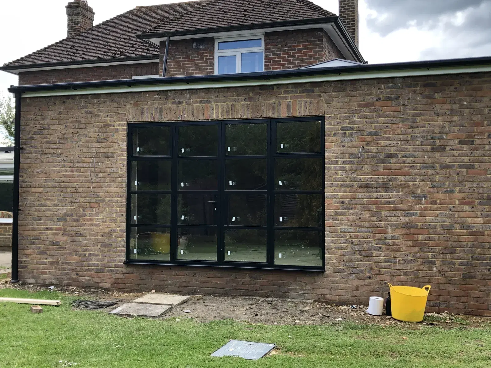 A four-leaf black bi-folding door set newly fitted into a brick wall, protective film still on the frames.