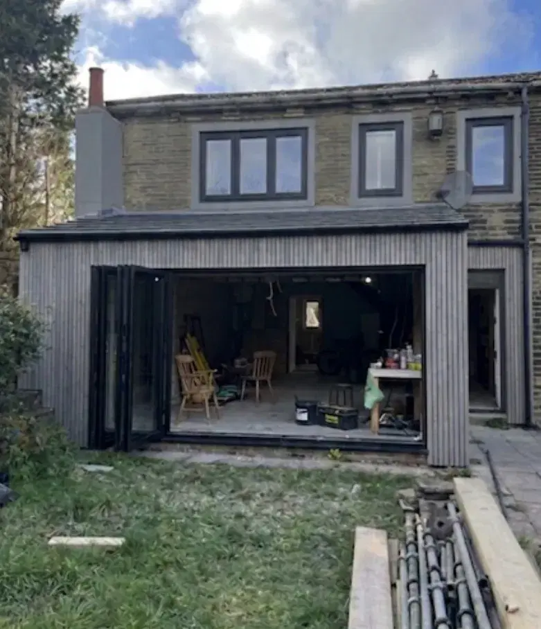 Bi-folding doors folded back on a timber-clad extension, opening onto a lawn.