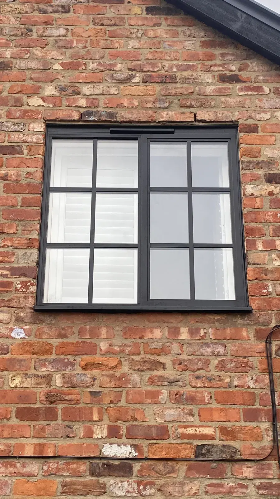 A black casement window with Georgian bars and white interior shutters, set in an old red-brick wall.