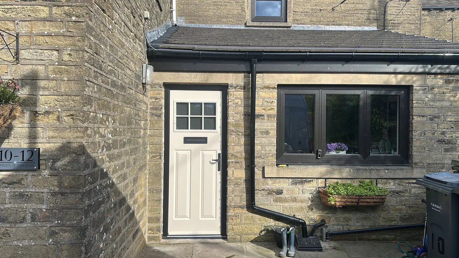 A cream composite door with a six-pane top light beside a black casement window on a stone cottage.