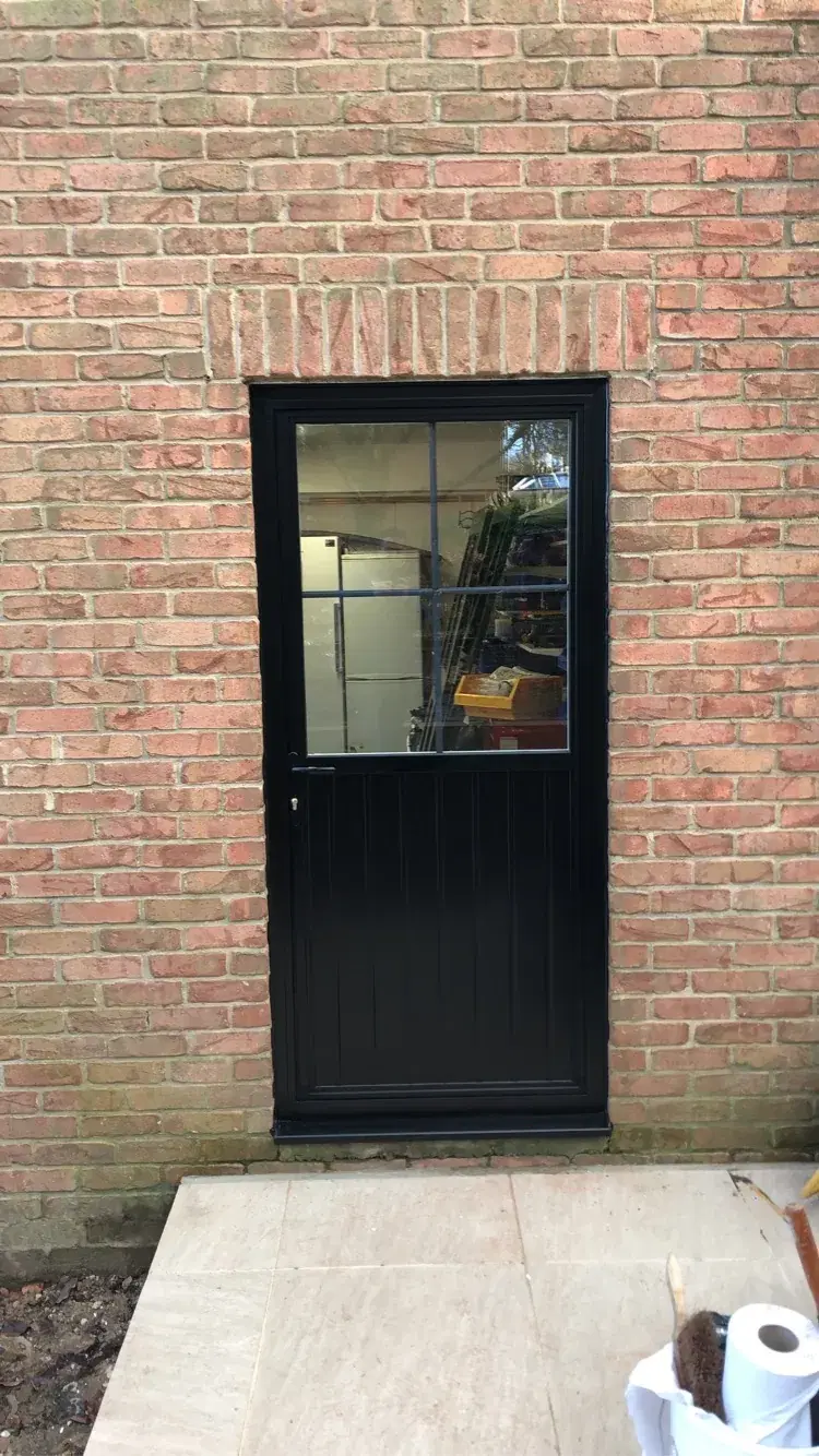 A black half-glazed back door with Georgian bars, fitted into a red-brick wall.