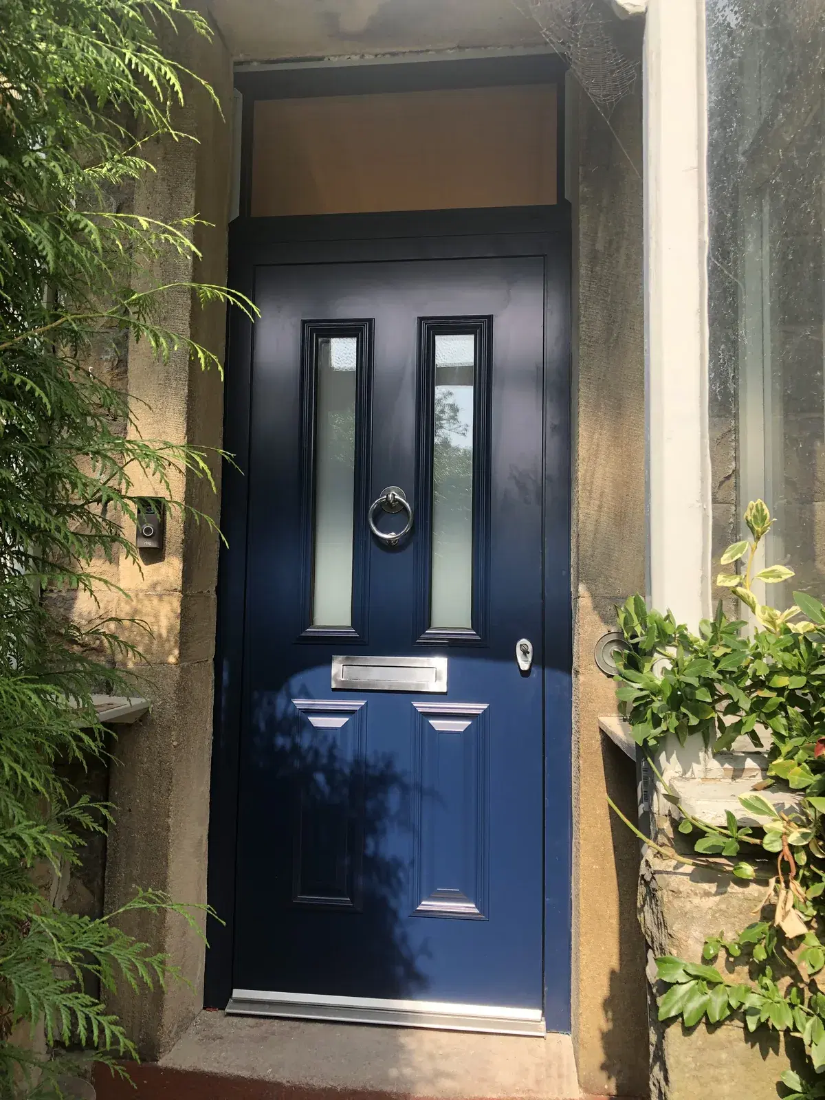 A navy blue four-panel composite door with a chrome ring knocker and letterplate, set in a stone porch.