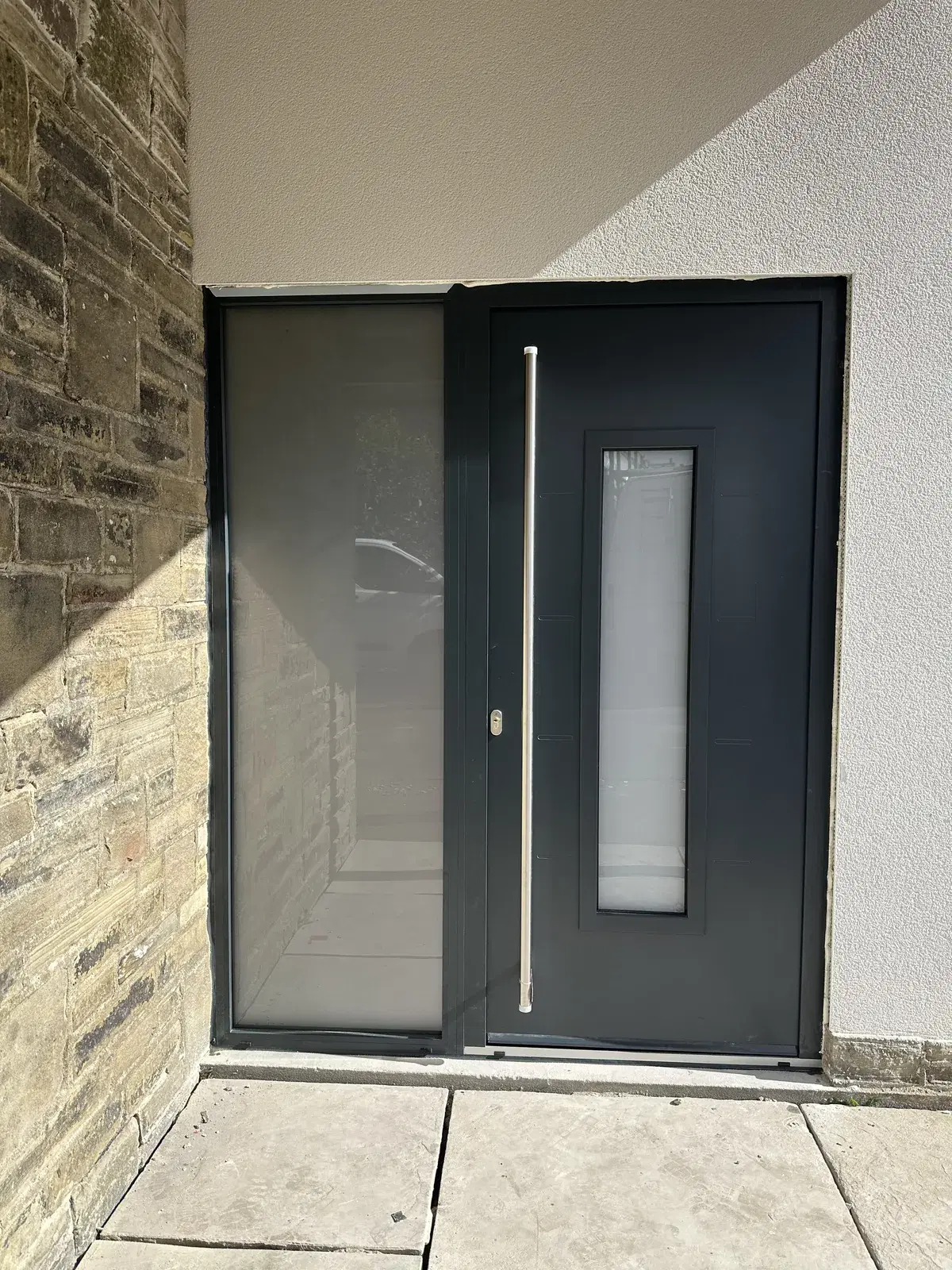 An anthracite entrance door with a slim vertical glazed panel and a full-height frosted side screen.