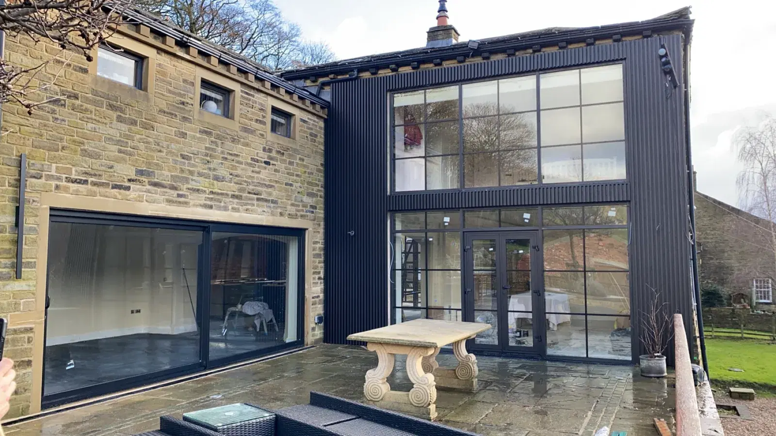 A stone house with black windows and a bi-folding door set in a single-storey extension.