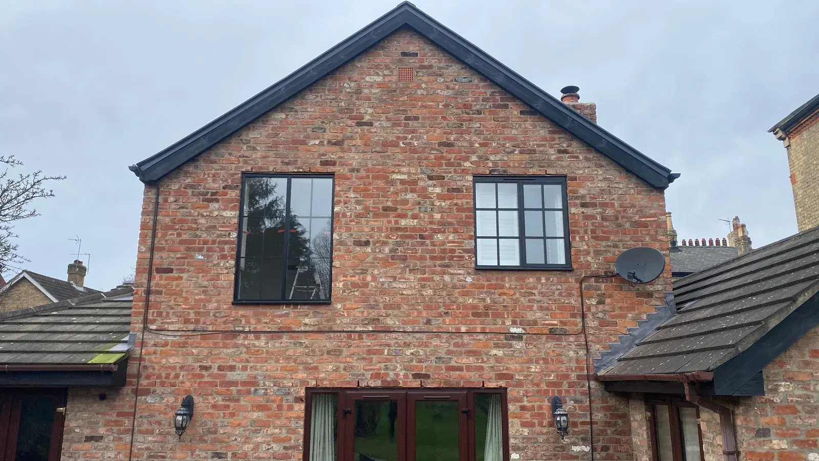 A red-brick gable fitted with dark grey heritage windows and glazed doors below.