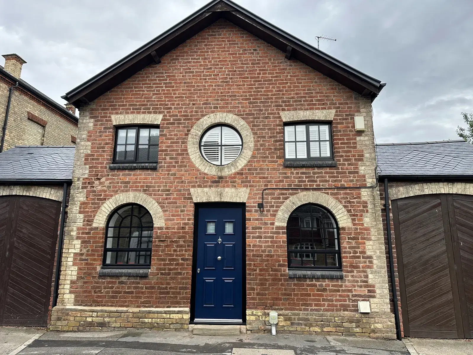 A converted red-brick mews building with heritage-style windows and a navy front door.