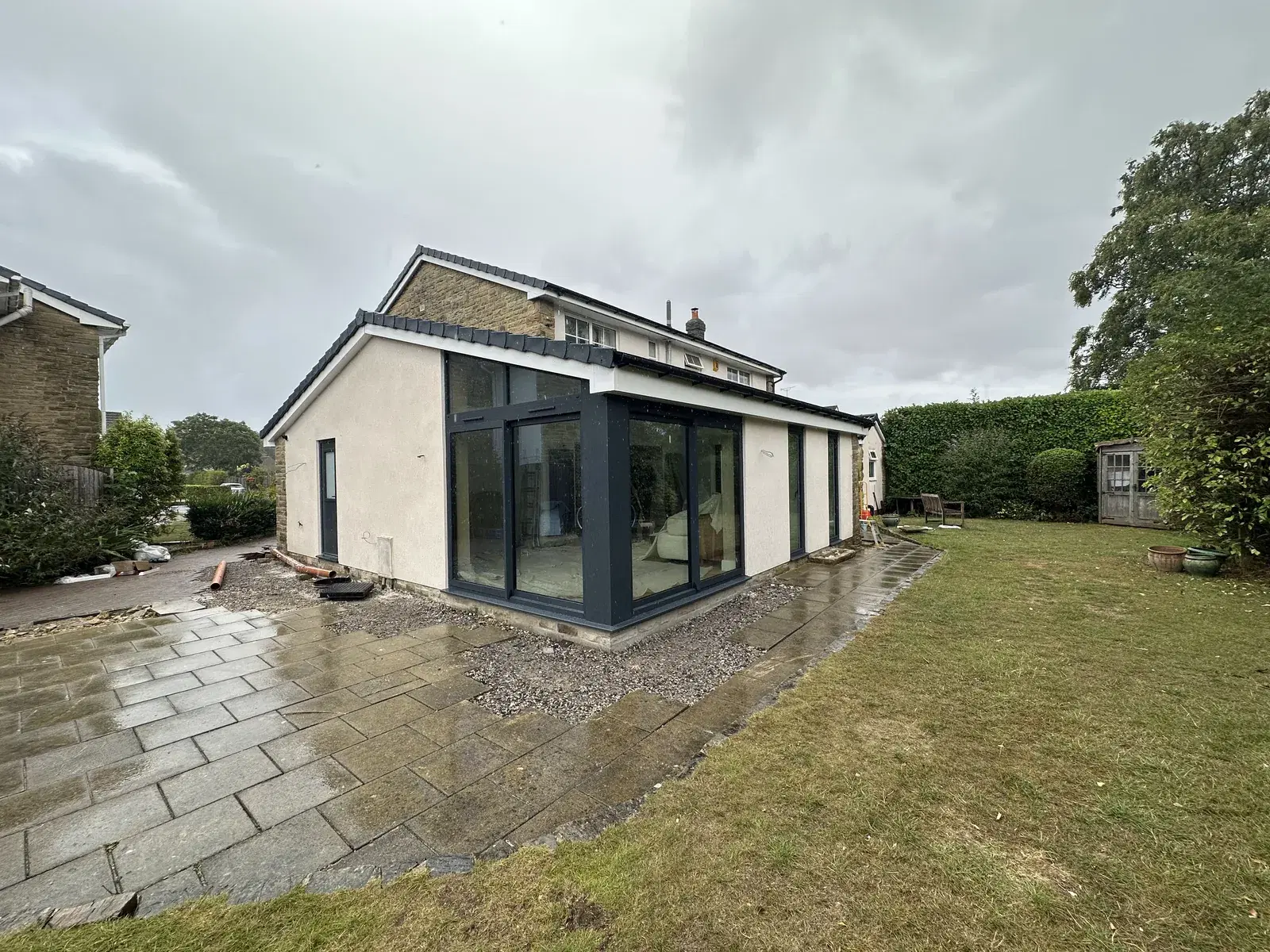 A rendered garden extension with dark grey sliding doors and corner glazing, seen from a wet patio.