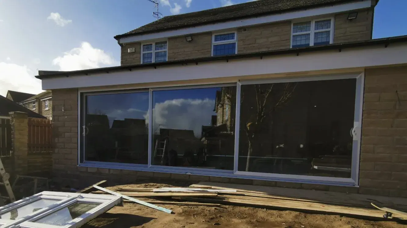 White-framed sliding patio doors spanning the rear of a stone extension on a bright winter day.