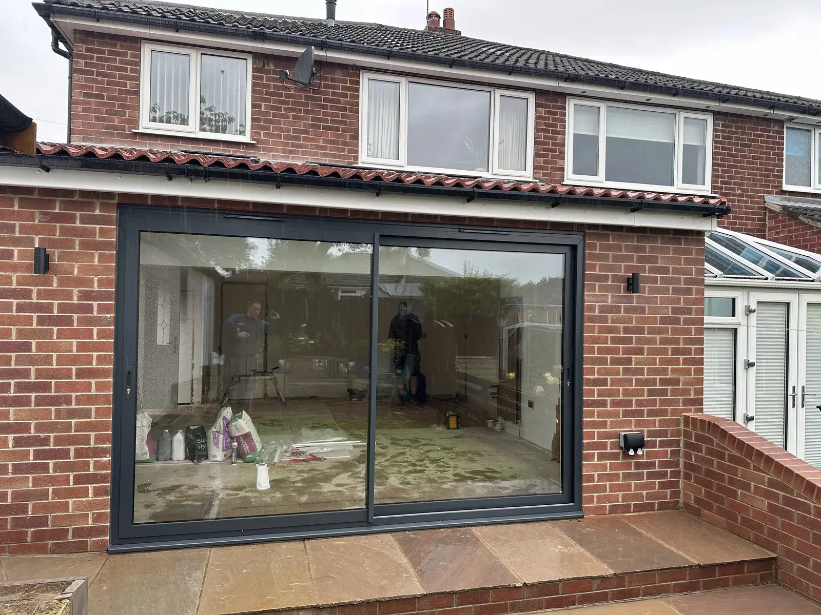 Anthracite sliding patio doors newly fitted into a red-brick rear extension, with the room still under construction.