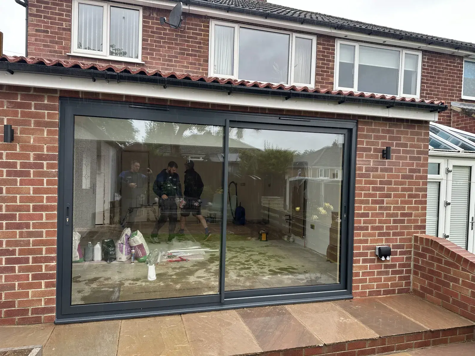A wide two-panel sliding door set in a red-brick extension, opening onto a sandstone patio.