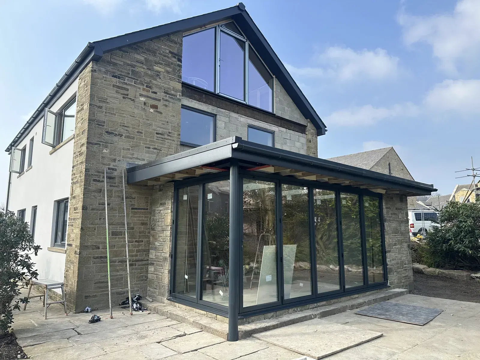 A stone and white-rendered home fitted with anthracite aluminium bi-folding doors beneath a flat canopy.
