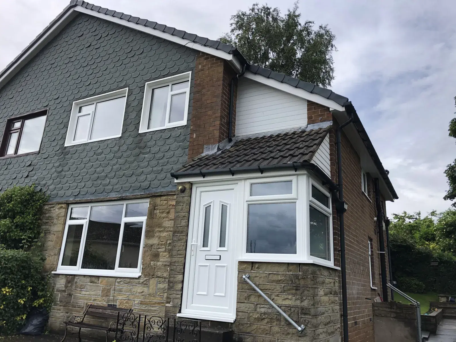 White UPVC casement windows and a bay window on a slate-hung and stone-built semi-detached house.