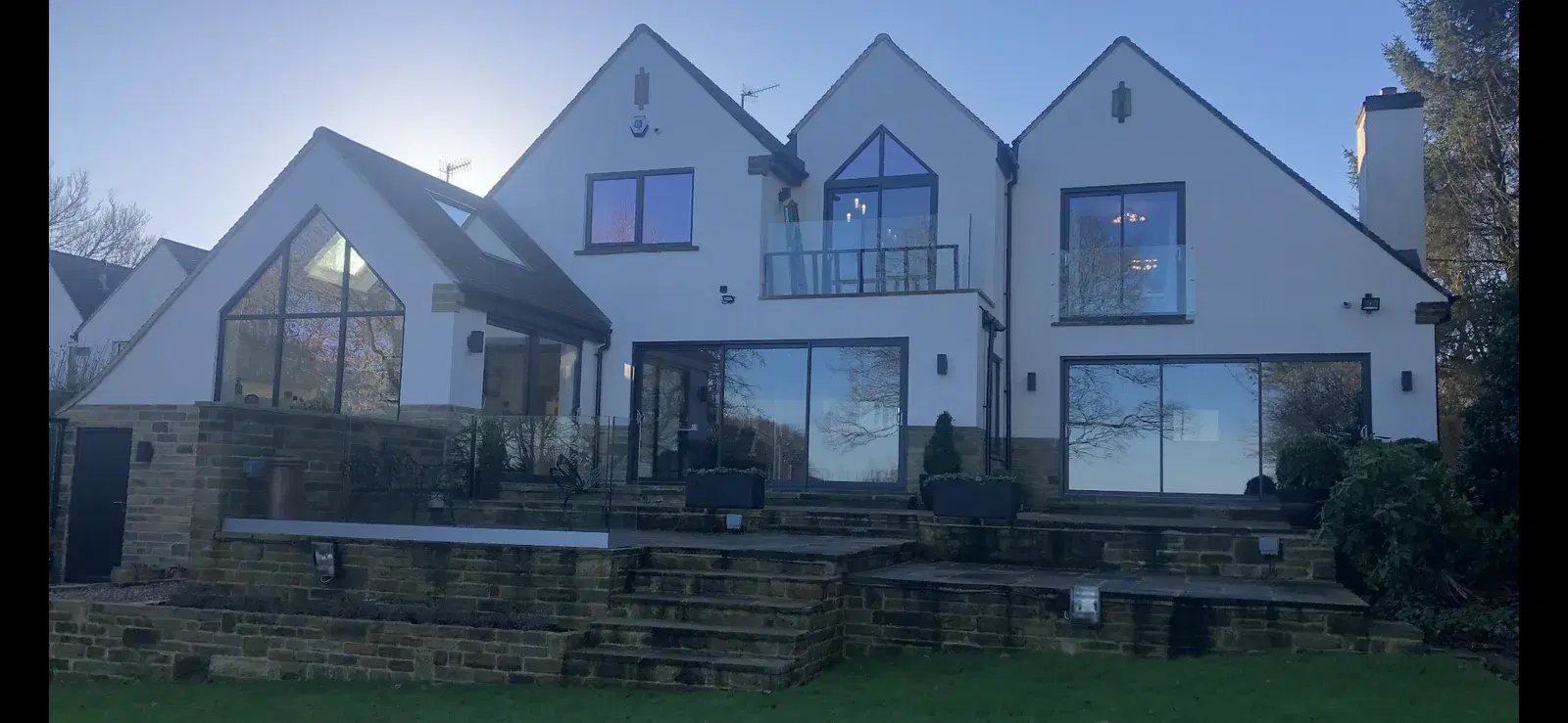 A large white-rendered house at dusk with full-height sliding doors and gable glazing.