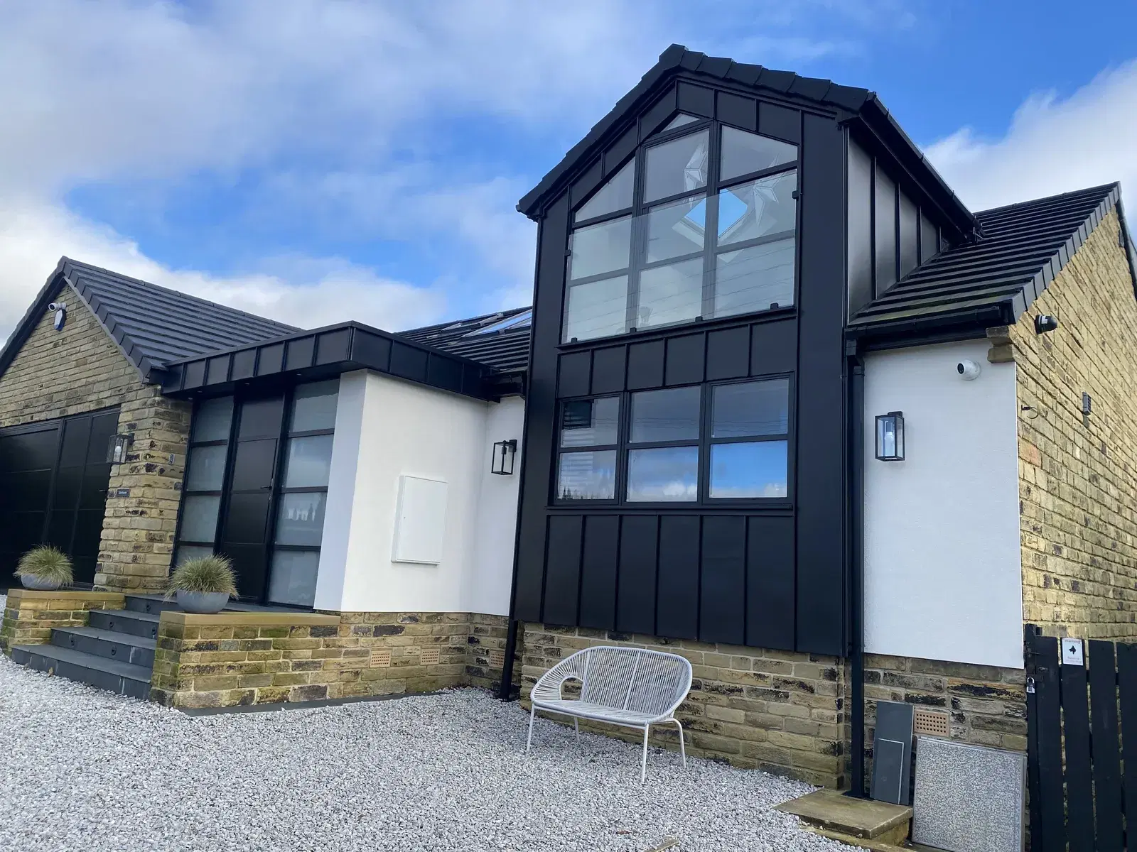 A stone-built house with black aluminium windows and a glazed garden room extension.