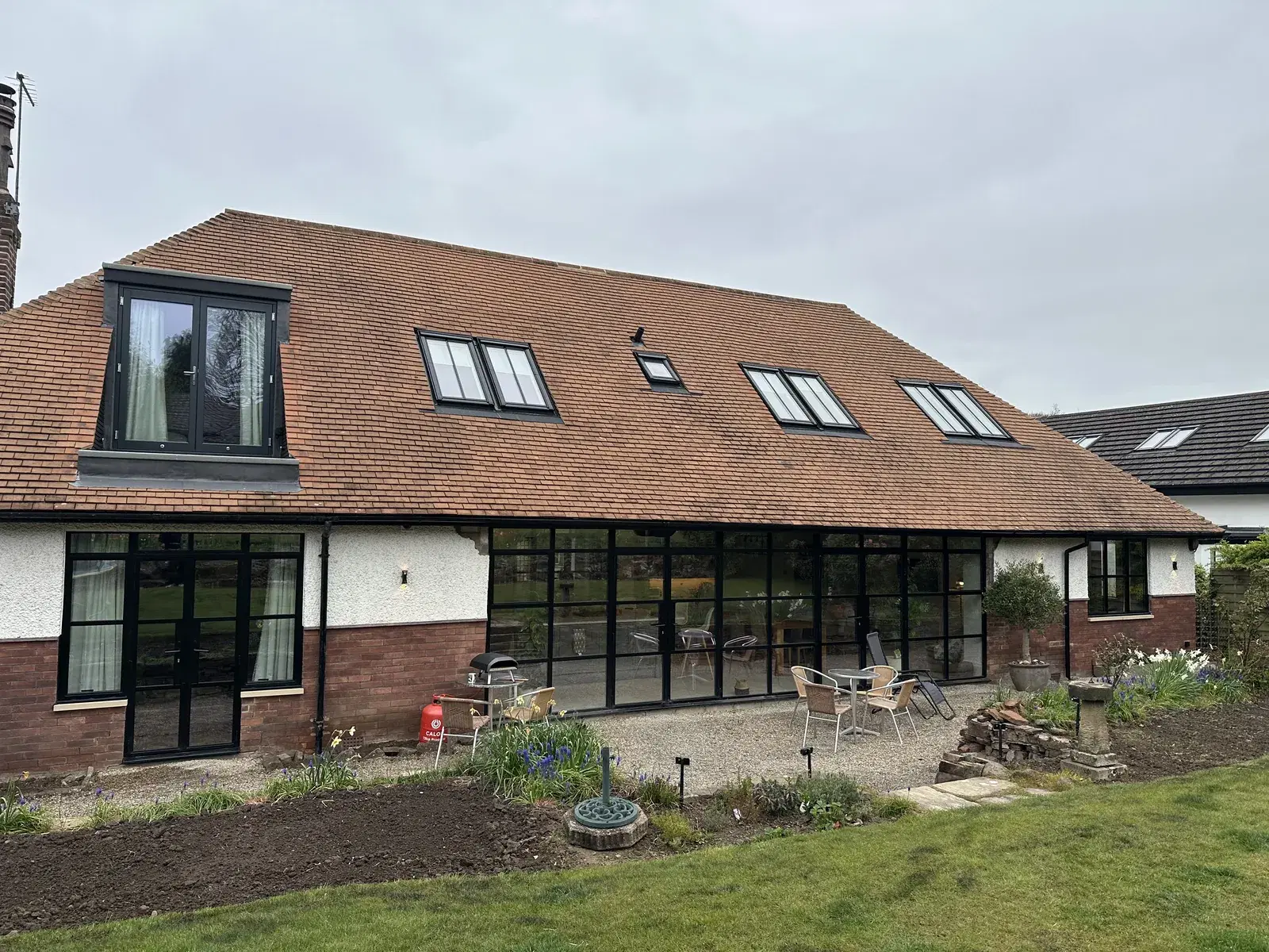 A tile-roofed barn conversion with black framed glazing running the length of the rear elevation.