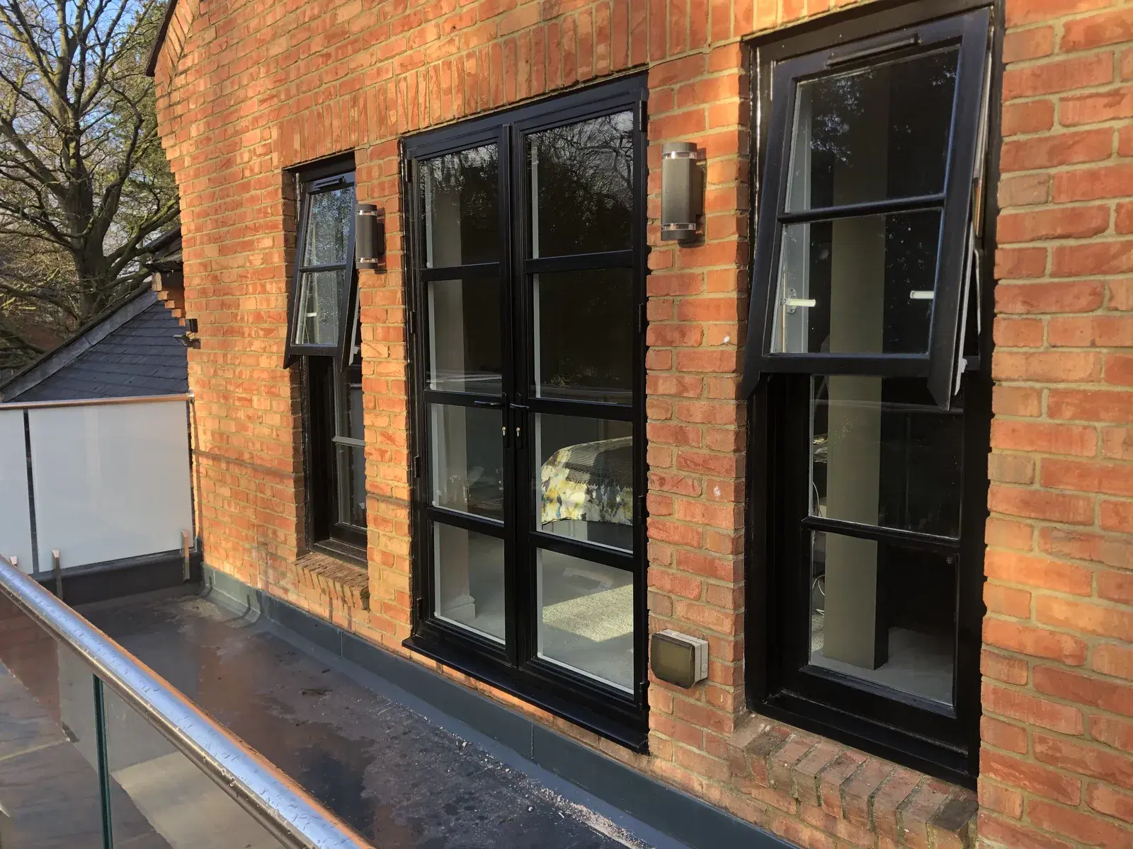 Black heritage-style windows with astragal bars and French doors on a red-brick period property.